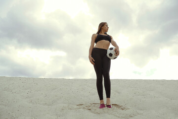 Bottom view of a sportive girl with a ball standing on the sand in the desert