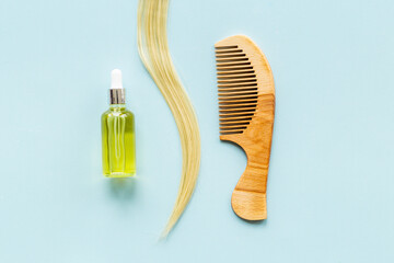 Essential oil for hair care with wooden hair comb and blond curl