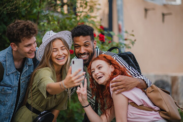 Portrait of group of young people outdoors on trip in town, taking selfie with smartphone.
