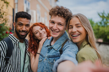 Portrait of group of young people outdoors on trip in town, taking selfie and looking at camera.