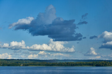 Gray cloud on a background of white clouds over a forest lake and forest
