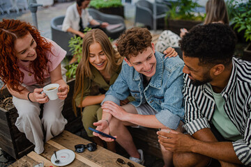 Group of happy young people sitting in outdoors cafe on town trip, talking.
