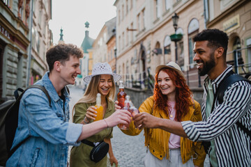 Front view of group of happy young people with drinks outdoors on street on town trip, laughing.