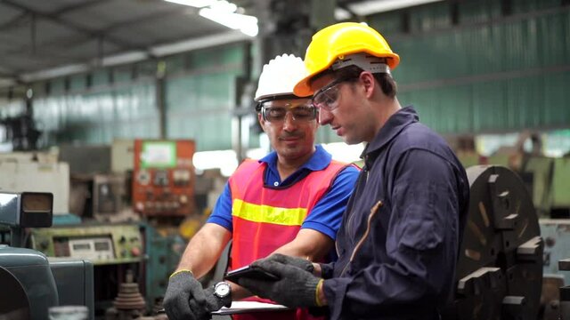 4K Confident man industry engineer and worker teamwork in safety helmet working together in heavy factory. Male foreman technician introduce factory department and metal machine work to senior manager
