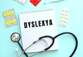 The text DYSLEXYA is written on a white notepad that lies next to the stethoscope and pills on a...