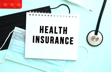 The text HEALTH INSURANCE is written in a notebook that lies on a blue background next to a medical masks