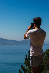 A boy taking photos and selfies during a hike in the mountains overlooking the sea