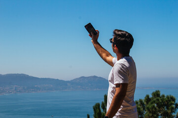 A boy taking photos and selfies during a hike in the mountains overlooking the sea