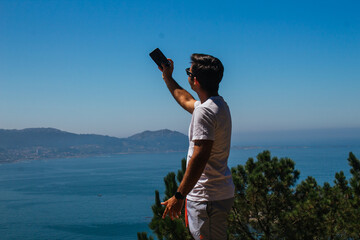 A boy taking photos and selfies during a hike in the mountains overlooking the sea