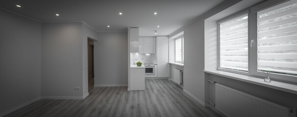 Modern bright interior of luxury studio apartment after renovation. White kitchen with fridge and oven. White walls. Beige parquet. Panorama view.