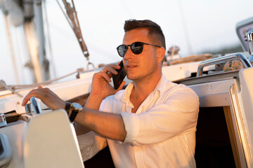 A successful man in a white shirt is talking on a mobile phone on a sailing yacht. As a concept of...