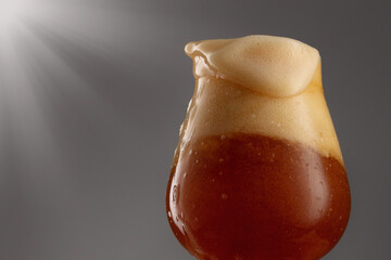 Glass of fresh and cold beer on a gray background. Detail of dark beer with overflowing foam head.