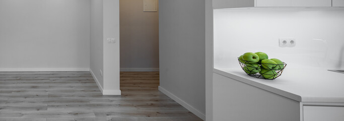 Contemporary interior of modern studio apartment without furniture. Green apples in vase. White walls. Parquet floor.