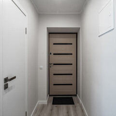 Modern light interior of apartment after renovation. Front view of wooden entrance door. White walls.
