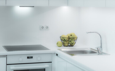 Modern interior of kitchen. White kitchen set with sink, oven and fridge. Green apples in vase on foreground.