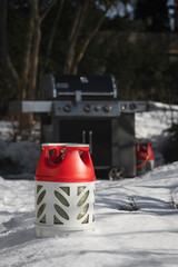 Composite gas cylinder of red and gray color and gas grill on the background