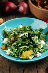 Green salad with oranges and mozzarella cheese on the wooden background