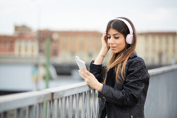 young brunette listening music by headphones in urban environment
