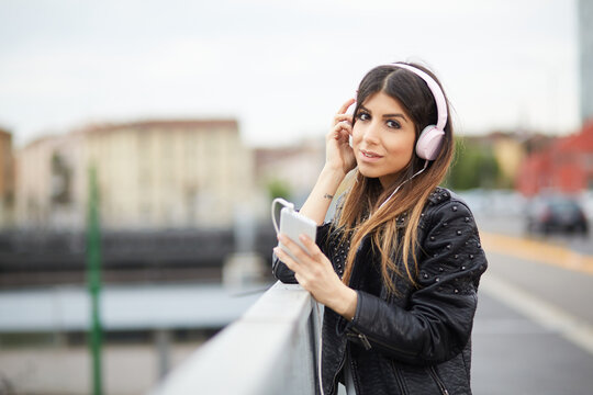 young brunette listening music by headphones in urban environment