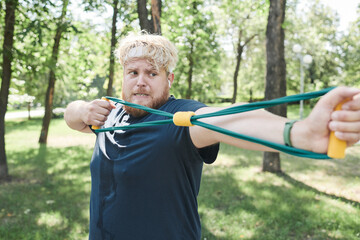 Overweight man exercising with sports equipment and doing stretching exercises during training in the park