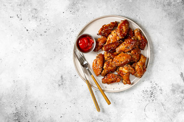 Homemade baked or fried chicken wings in barbecue sauce in a plate on a light gray cooking table...