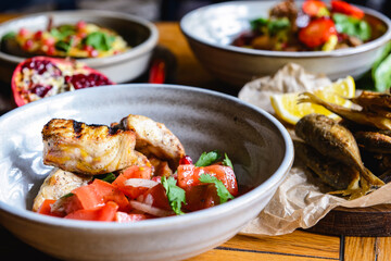A dinner of fish and tomato salad served in a bowl on the table with other dishes.
