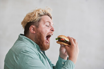 Overweight man opening his mouth and eating fast food against the white background