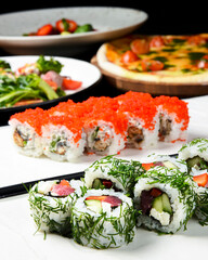 Sushi rolls with tuna, cucumber and cream-cheese in chopped dill. Served on a white plate over white background.