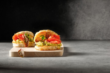 Avocado and salmon bruschetta starter crostini on bread with cucumber on wooden board and dark background