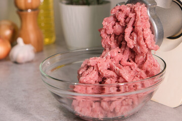 Minced meat grinder on the kitchen table in a transparent bowl. - 452486338