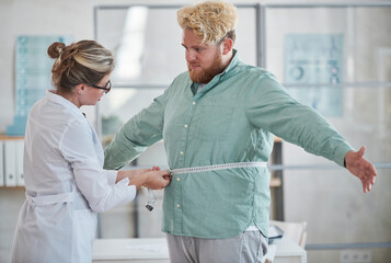 Young nutritionist measuring the overweight man with centimeter tape and prescribing a diet
