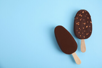 Ice cream bars glazed in chocolate on light blue background, flat lay. Space for text