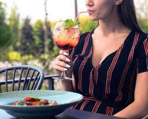 Young woman eating salad with strawberries and drinking aperol spritz cocktail in outdoor restaurant. Eat out concept