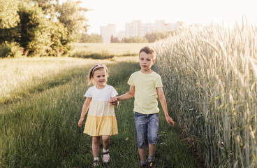 A boy and girl brother and sister play in the field in the summer. Happy summer vacation. Boy and girl on country road. Wheat field