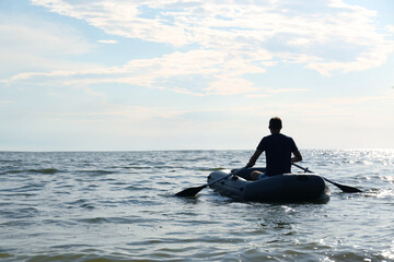 Man rowing inflatable rubber fishing boat on sea, back view. Space for text