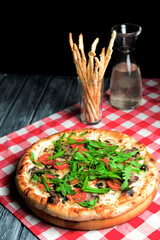 Rustic tasty pizza with meat, mushrooms, tomatoes and basil. Over wooden table and black cloth, photo in dark tones.