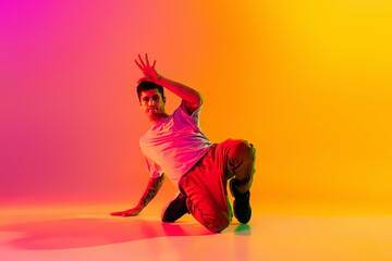 Caucasian man, break dancing dancer ptacticing in casual clothes isolated over gradient pink yellow background at dance hall in neon light.