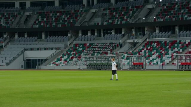 ZOOM OUT Caucasian pre teen kid boy entering the field of huge soccer stadium, holding a ball, dreaming of becoming professional player, soccer star
