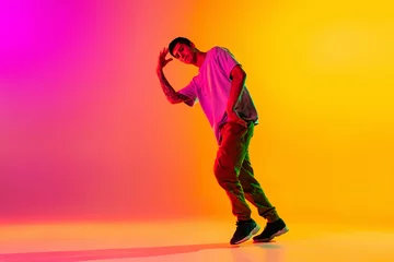 Poster Full length portrait of young stylish man, break dancing dancer in casual clothes isolated over gradient pink yellow background at dance hall in neon light. © master1305