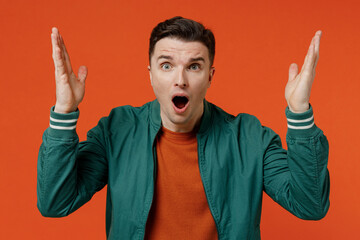 Angry shocked unnerved aggrieved disconcerted young brunet man 20s wear red t-shirt green jacket spreading hands isolated on plain orange background studio portrait. People emotions lifestyle concept
