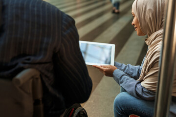 Muslim woman and disabled man using tablet computer together