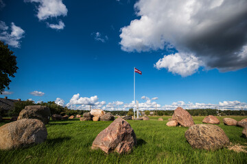 Memorial place with large stones. A flowing Latvian flag on a long mast.