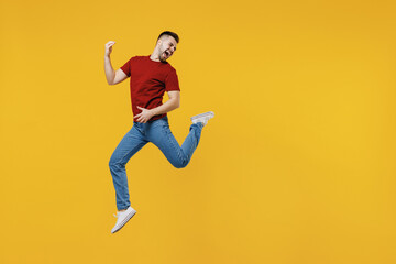 Fototapeta na wymiar Full length overjoyed expressive fun happy young man wear red t-shirt casual clothes jump high playing guitar isolated on plain yellow color wall background studio portrait. People lifestyle concept.