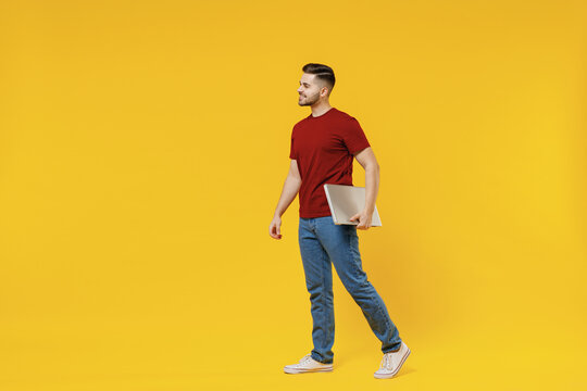 Full Length Smiling Happy Young Man In Red Tshirt Casual Clothes Hold Closed Laptop Pc Computer Work Look Aside Isolated On Plain Yellow Color Wall Background Studio Portrait People Lifestyle Concept