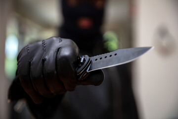 Burglar with balaclava, holding a knife in gloved hand,