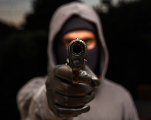 Hooded thief holding a pistol, street at night background,