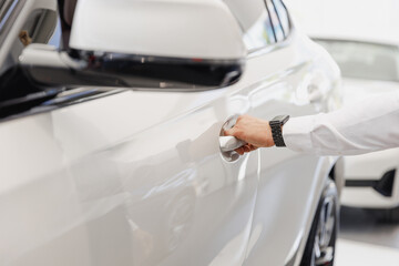 Obraz na płótnie Canvas Close up man male hand arm customer buyer client in white shirt chooses auto want to buy new automobile open car door handle in showroom vehicle salon dealership store motor show indoor Sales concept