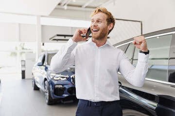 Naklejka na ściany i meble Man excited customer male buyer client wear white shirt talk by mobile cell phone advise choose auto want buy new car automobile in showroom vehicle dealership store motor show indoor. Sales concept