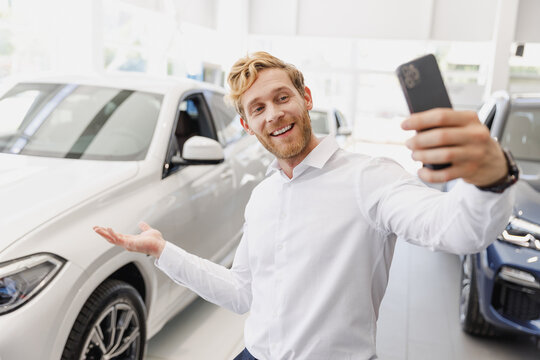 Man customer male buyer client in white shirt do selfie shot on mobile cell phone show car choose auto want buy new automobile in showroom vehicle dealership store motor show indoor. Sales concept