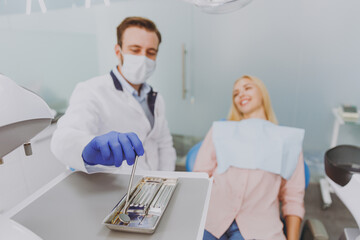Young caucasian man dentist doctor taking intruments examine mouth cavity of patient woman sitting at dentist office chair indoor cabinet near stomatologist Healthcare caries treatment Focus on tools
